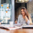 Portrait Of Smiling Female Office Worker Writing Looking At Camera Sitting At Conference Room During The Meeting