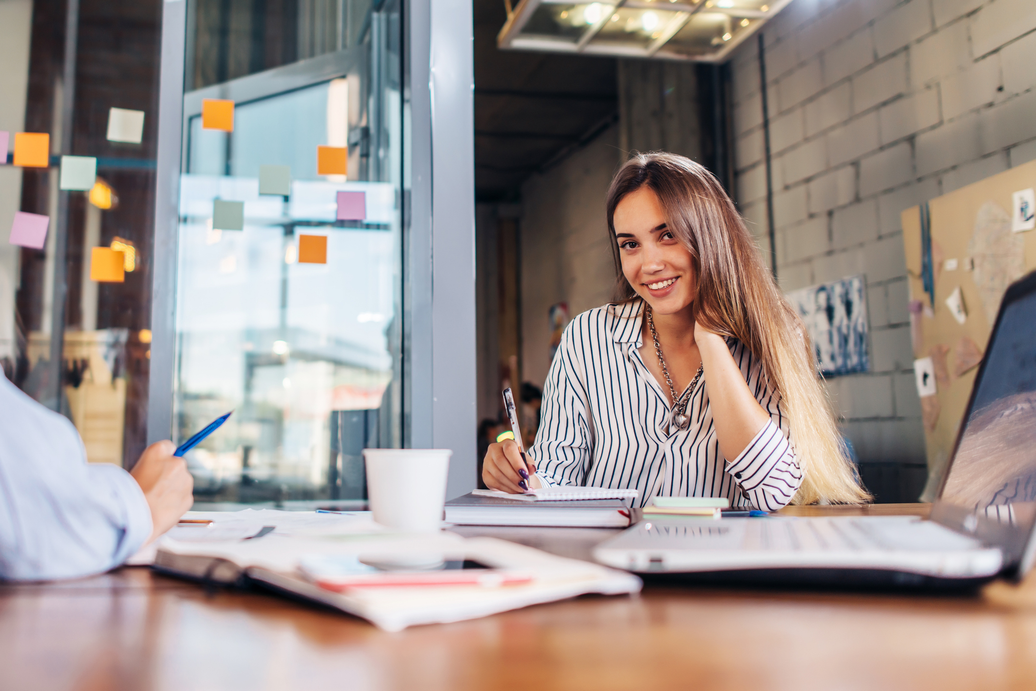 Portrait Of Smiling Female Office Worker Writing Looking At Camera Sitting At Conference Room During The Meeting